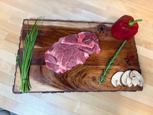 A bone in pork steak on a board of garnishments