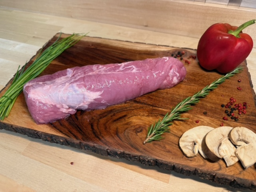 A pork tenderloin roast on a board of garnishments