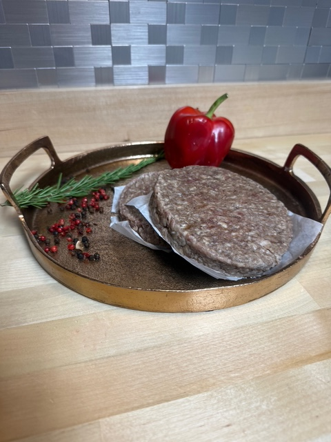 Two Wagyu beef patties on a tray with pepper seeds, rosemary, and bell pepper used as garnishment