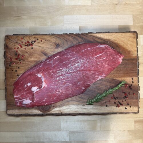 A Large flank steak on a cutting board of garnishments
