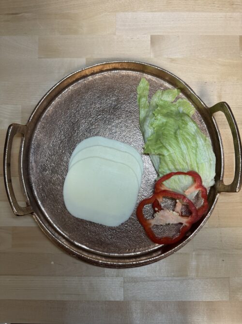 Three slices of mozzarella cheese on a tray with two slices of bell pepper and lettuce used as garnishment